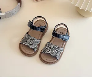 Detalle de sandalias negras de charol para niña con tiras trenzadas de pedrería y velcro