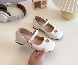 Dettaglio delle scarpe Mary Jane bianche con logo a fiore dorato e ciondolo di strass