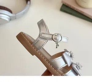 Detail van zilveren meisjessandaal met strass-strik en sterretje aan de gespband