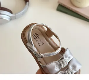 Detailopname van zilveren meisjessandalen met glanzende strass-strik en klittenbandsluiting