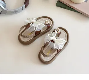 Detail of girls' sandals featuring faux pearls and lace bows on a soft beige background