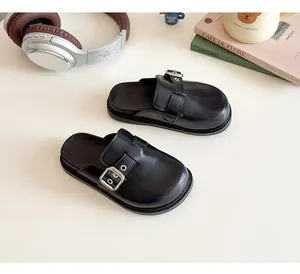 Dettaglio dei sabot in pelle nera da bambina con fibbia quadrata d'argento su una rivista
