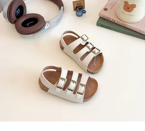 Gros plan de sandales enfant crème avec boucles métalliques et semelle aspect liège