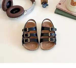 Détail de sandales noires pour enfants avec trois brides à boucles dorées et semelle liège