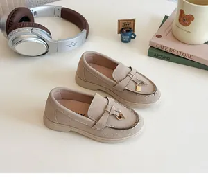 Close-up of beige suede kids loafers featuring a golden lock charm and moccasin stitching