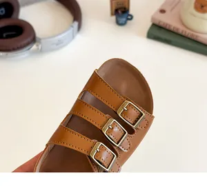 Gros plan de sandales en cuir marron pour enfants avec trois brides et boucles dorées