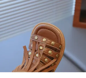 Détail rapproché de sandales marron pour filles avec franges cloutées et semelle tressée