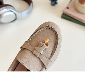 Detail of apricot suede kids loafers featuring golden metal buckle and white stitching