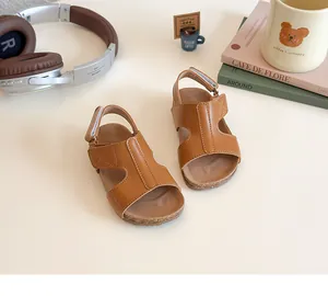 Close-up of brown leather girl's sandals with hollow straps and velcro on a creamy base