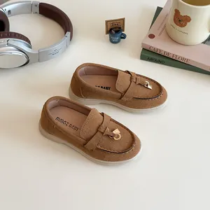 Brown suede kids loafers with gold metal buckle on a minimalist decorative background