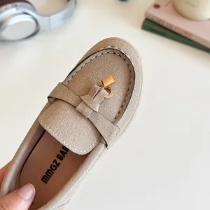 Beige suede loafers for children featuring a stylish gold padlock detail on a white desk