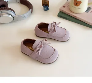Flat lay of soft pink suede baby loafers with bow detail on a minimal background