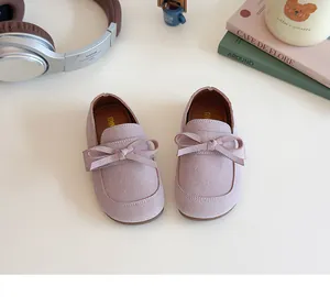 Close-up of girls' lavender suede princess shoes with bow detail on a beige table