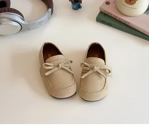 Overhead detail view of beige suede kids princess shoes with a bow on a white desk