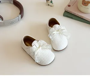 Close-up of white girls' leather shoes with delicate lace bow and embossed texture