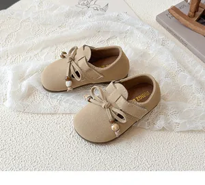 Detail of camel suede girls' flat with bow decoration and wooden bead on lace background