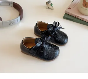 Detailed view of girls black Mary Jane shoes with lace bow and woven texture detail