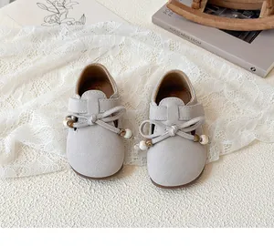 Detailed view of grey suede girls' shoes with beaded bow on a white lace fabric background