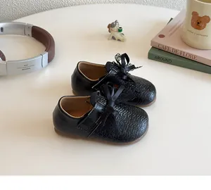 Detailed view of girls' black leather Mary Janes featuring delicate lace bow and textured finish