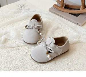 Detailed top view of beige suede girls' bow shoes with beads on a decorative background