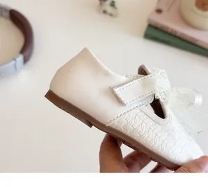 Close-up of white girls princess shoes with lace bow, velcro strap, and textured toe