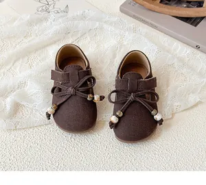 Detailed top view of brown suede girls' flat shoes with a bow and marble beads