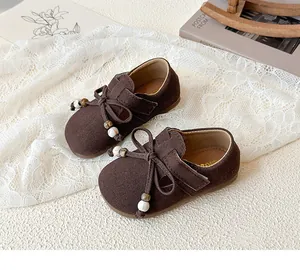Detail of brown suede girls princess shoes with bow and pearl beads on lace background