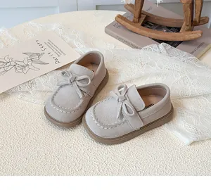 Detail of children's beige suede loafers with bow knot and white contrast stitching