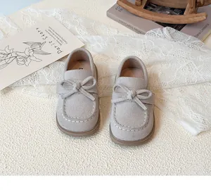 Detail of beige children's moccasins featuring a bow and white hand-stitched seams