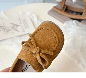 Macro view of children's suede loafers featuring a bow tie knot and fine stitching detail