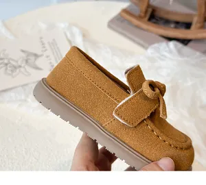 Detailed macro view of caramel suede kids' loafers featuring bow knot and velcro strap