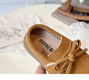 Detail of children's brown suede loafers featuring a decorative bow and stitching