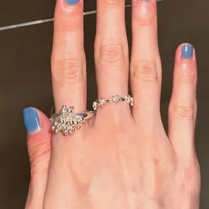 Detailed view of silver fireworks and floral rings worn on fingers with blue nail polish