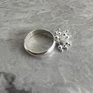 Macro view of silver firework flower ring with clustered tassel pendant on marble background