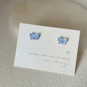 Makroaufnahme schillernder blau-violetter Schmetterling-Ohrstecker auf weißer Karte