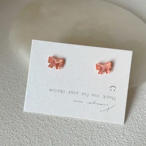 Makroaufnahme kleiner rosa irisierender Schmetterlings-Ohrstecker auf weißer Karte