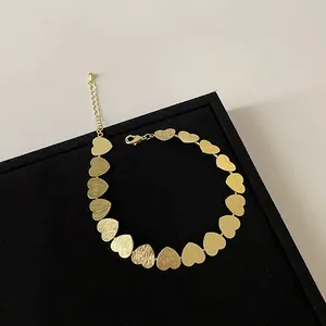Detalle de pulsera de corazones dorados con texturas metálicas cepilladas y pulidas