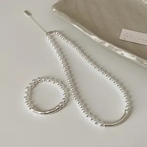 Elegantes Set aus Perlenkette und Armband mit mattem Silbermetall auf einem Keramiktablett
