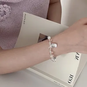 Detail eines Perlenarmbands mit Kristallperlen und quadratischem GOOD Anhänger am Handgelenk