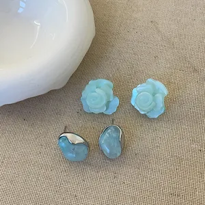 Set orecchini a camelia blu menta e design irregolare su sfondo di tessuto lino