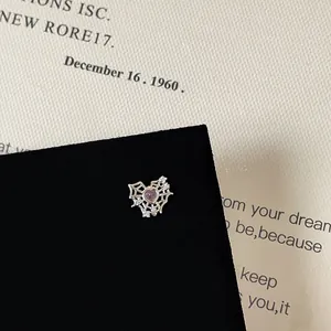 Macro shot of heart-shaped spider web stud earrings with pink gemstone and silver finish