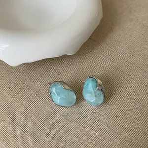 Dettaglio di orecchini a lobo camelia blu chiaro con montatura in argento su tela beige