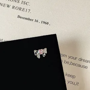 Detailed view of silver bow stud earring with pink heart zircon on a black card