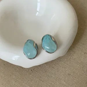 Dettaglio degli orecchini a lobo camelia blu in un piatto di ceramica bianca su lino