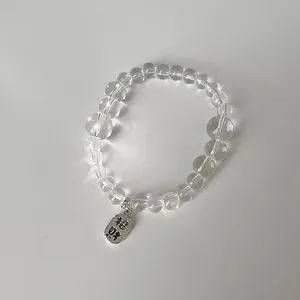 Nahaufnahme des transparenten Perlenarmbands mit silbernem Glücksbringer-Anhänger