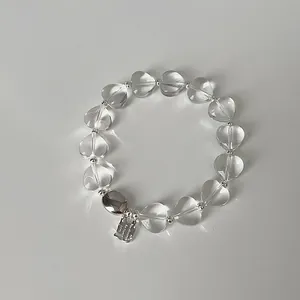 Detailansicht eines klaren Herzperlen-Armbands mit silbernem Logo-Anhänger aus Metall