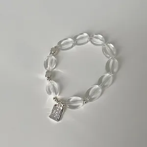 Makrodetail von klaren Kristallperlen und einem rechteckigen Metallanhänger am Armband