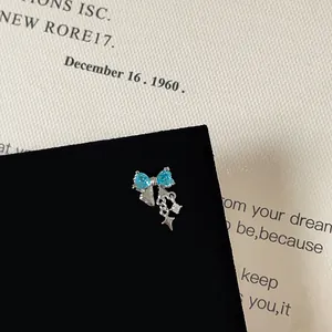 Close-up of blue zircon bow earring with star pendant and silver chain detail