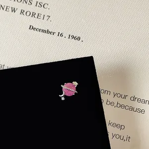 Close-up of pink zircon planet stud earring with silver star and moon details on black card