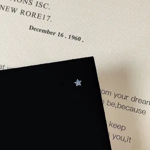 Close-up of small light blue flower stud earring with silver claw on a vintage page